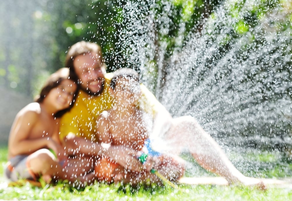 Father having fun with his little sons holding water sprinkler