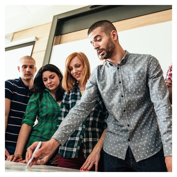 A teacher stands with three students as they look at a math problem